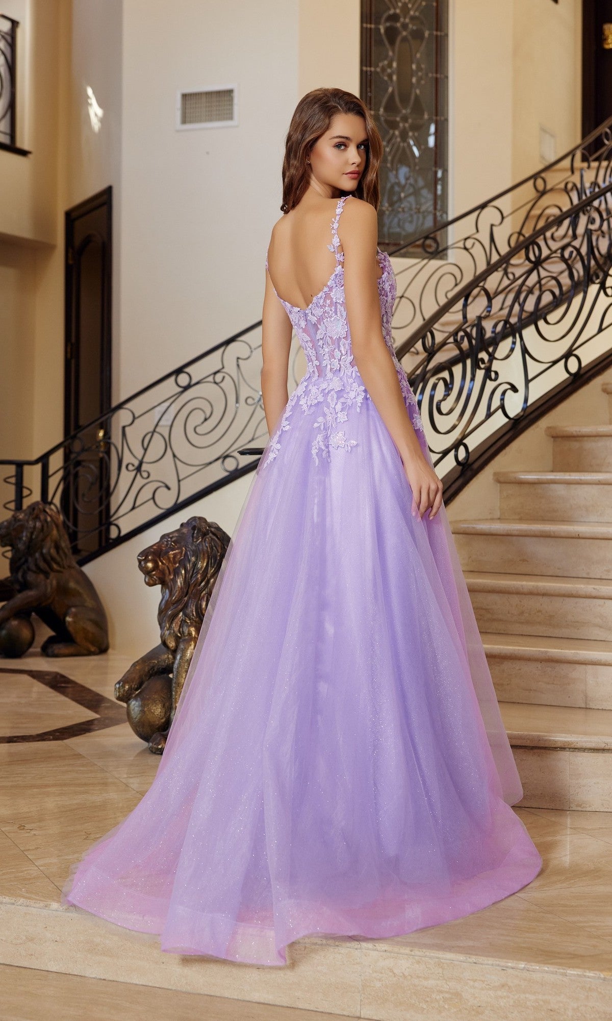 A woman wears the Nox Anabel R1824 long lavender prom dress with a sleeveless floral embroidered corset and tulle A-line skirt, standing on marble stairs with ornate railing and lion statues in an elegant interior.